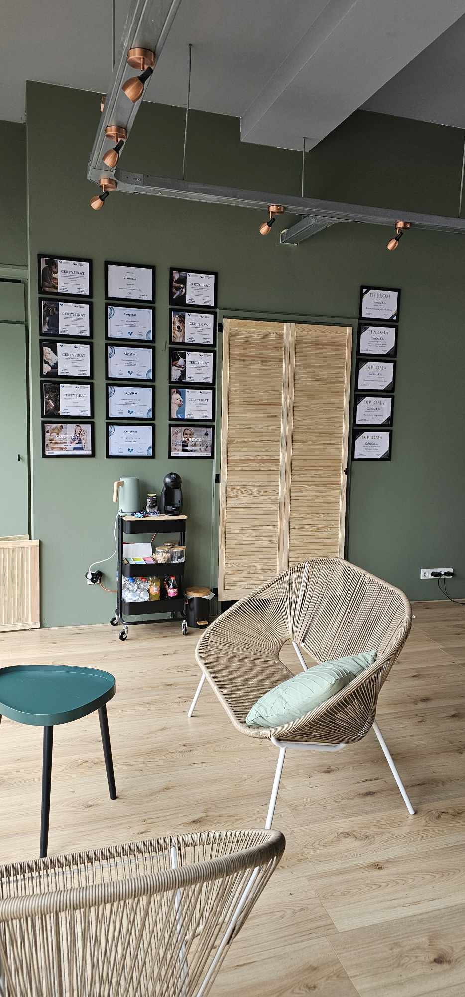 De zithoek in de salon: groene wand met ingelijste certificaten, rotan stoelen en een houten deur
